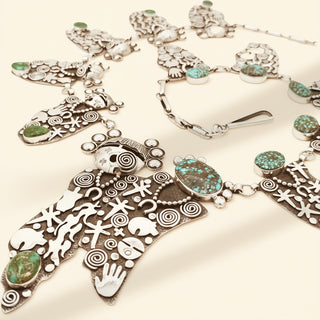 Silver necklace with intricate designs and turquoise stones on a beige background