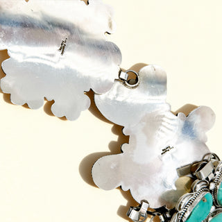 Close-up of a necklace with white shell-like pendants and silver and turquoise accents.