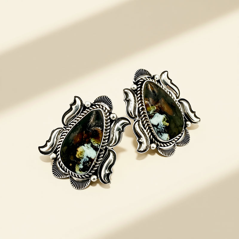 Pair of ornate earrings with gemstone-like centers on a beige background