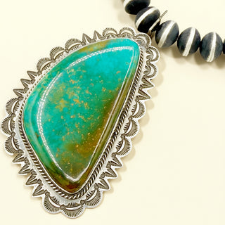 Turquoise stone pendant with silver frame on a beige background