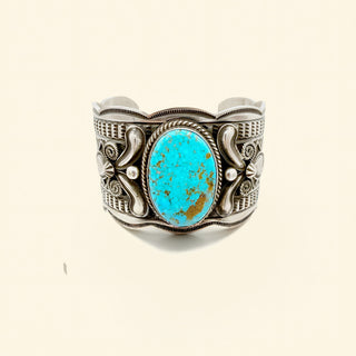 Silver cuff bracelet with a turquoise stone on a beige background