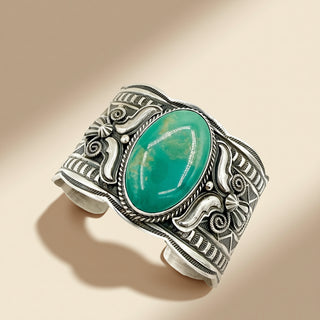 Decorative silver bracelet with a green stone on a beige background