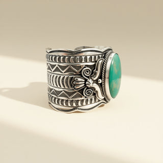 Silver cuff bracelet with intricate designs and a turquoise stone on a beige background