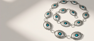 A silver-toned jewelry piece featuring multiple flower-shaped links with turquoise blue centers, arranged in a spiral on a light beige background.