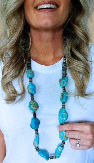 Woman wearing a long turquoise beaded necklace against a beige background