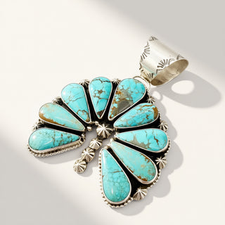 A sterling silver pendant featuring a fan arrangement of turquoise stones with brown matrix veining, set in a silver bezel with a matching silver wrap band, photographed on a clean white background with soft shadows.