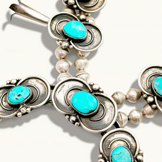 A close-up of a silver-toned necklace with multiple oval turquoise stones and small silver beads, shown on a plain light background.