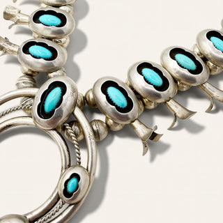 A close-up of a silver-toned jewelry piece featuring multiple oval turquoise inlays set against black enamel, with curved silver bands and small floral-like extensions.