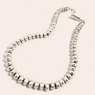A silver beaded necklace with polished, rounded disc-like beads and a lobster clasp, displayed on a light beige background.