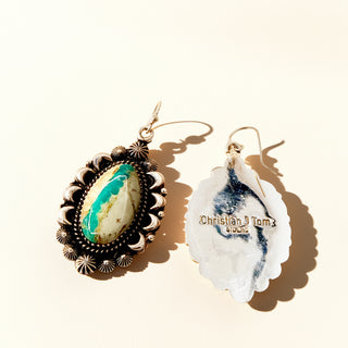 Pair of earrings on a beige background, one earring with a green stone and gold accents, the other with a silver stamp.