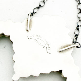 Close-up of a silver necklace with a leaf-shaped pendant on a white background