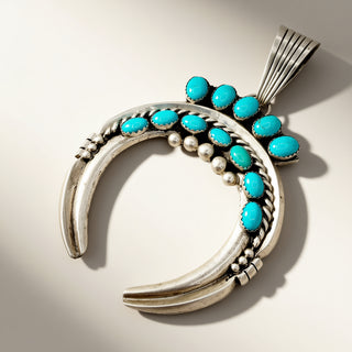 A silver crescent-shaped pendant necklace featuring multiple oval turquoise stones and small silver beads, photographed on a clean light beige background.