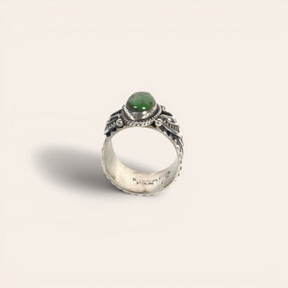 Silver ring with a green gemstone on a light beige background