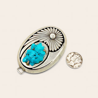 Silver pendant with turquoise stone and coin on a beige background