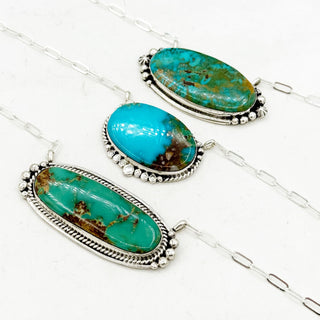 Turquoise stone pendants on silver chains against a white background