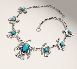 Multiple silver birds with turquoise stones on a handmade chain sitting on a cream background