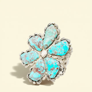 Turquoise flower-shaped cuff with silver accents on a beige background