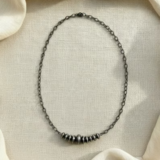 A sterling silver necklace with a graduated saucer-shaped bar pendant on a chain, displayed against a cream background.