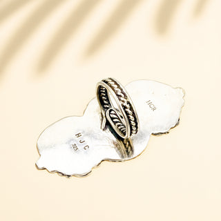 Silver ring with  design on a white stone with 'HJC' engraving, against a beige background