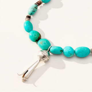 turquoise beaded necklace with silver pendant on a beige background