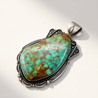 A Southwestern-style sterling silver pendant featuring a large, polished turquoise stone with brown matrix veining, set against a clean white background.