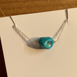 Necklace with a blue pendant on a white card, placed on a wooden surface.