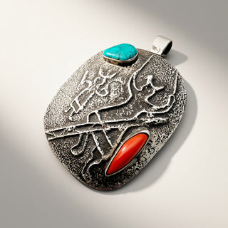 A textured sterling silver pendant featuring a turquoise cabochon and an oval red coral inlay, displayed on a clean light gray background.