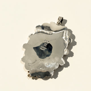 Silver pendant with a textured surface on a beige background