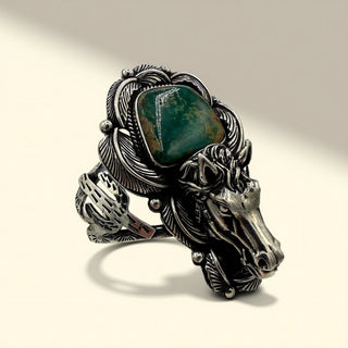 Silver cuff with horse design and green stone on a beige background