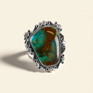 Ring with a large turquoise stone and silver decorative band on a beige background