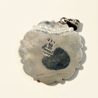 Silver pendant with engraved design on a beige background