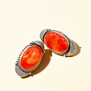 Pair of earrings with orange stone and silver frame on a beige background