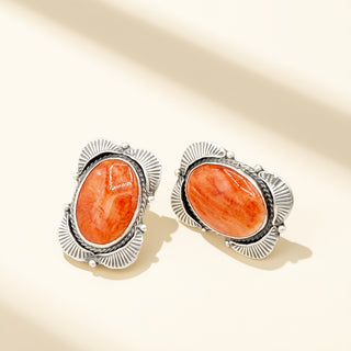 Pair of earrings with orange stones and silver frames on a beige background