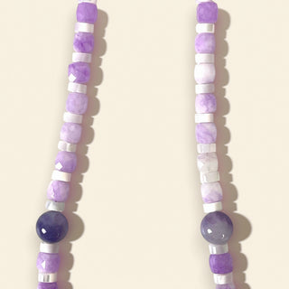 Two beaded necklaces with purple and white beads on a beige background