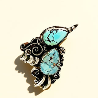 Turquoise stone ring with intricate silver design on a beige background