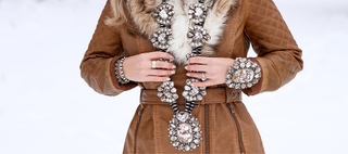 Person wearing a brown coat with fur collar and a decorative scarf on a white background