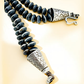 Black beaded necklace with silver floral clasp on a beige background