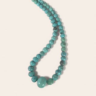 Turquoise beaded necklace on a light pink background