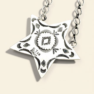 Star-shaped silver pendant with intricate patterns on a beige background
