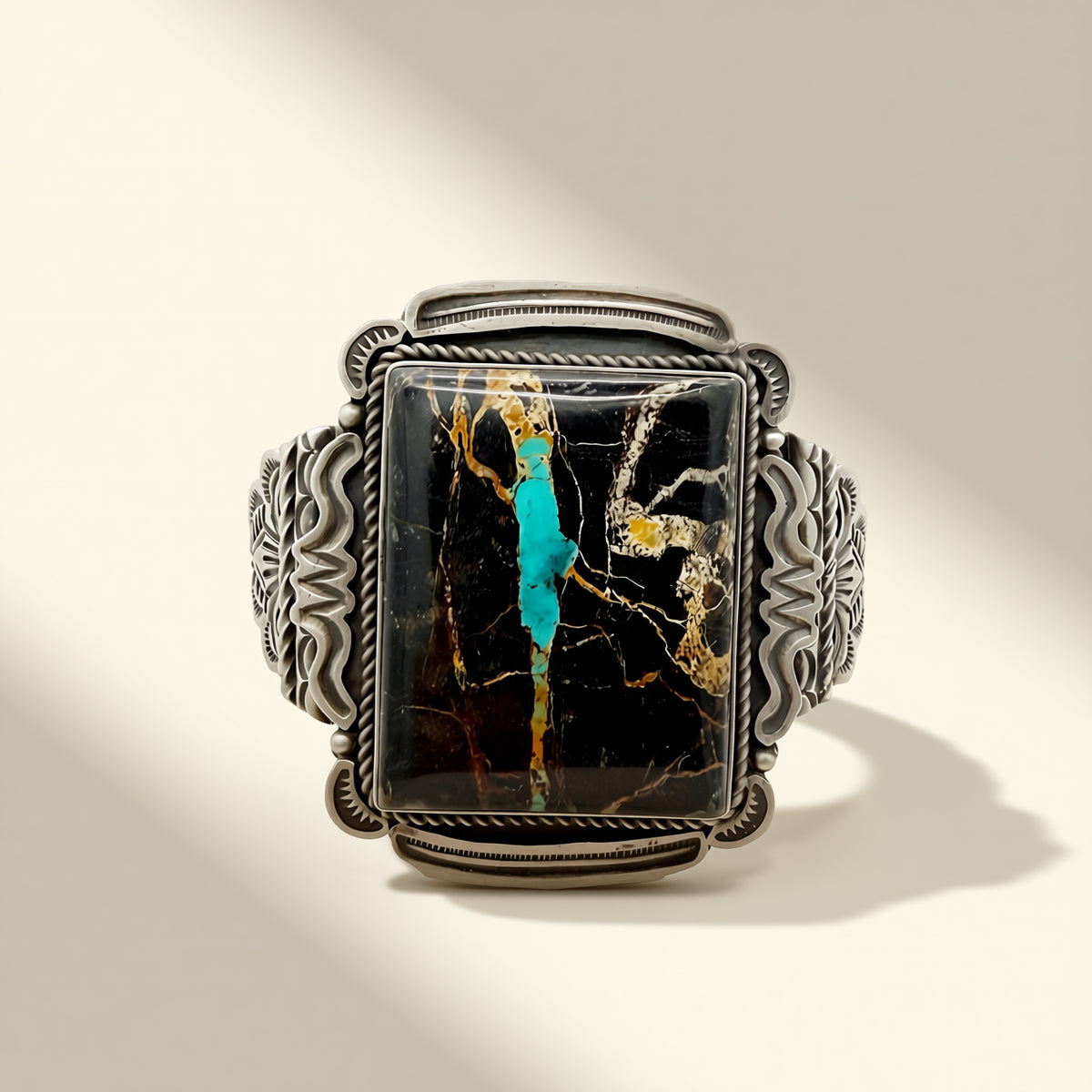 Silver cuff with a rectangular stone featuring black, gold, and turquoise colors on a beige background