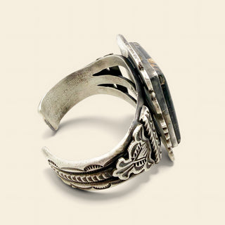 Close-up of a silver cuff with intricate designs on a beige background