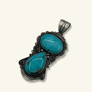 Turquoise stone pendant with intricate black metalwork on a light beige background