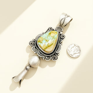 Silver pendant with a yellow stone next to a quarter on a beige background