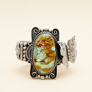 Silver cuff with butterfly design and turquoise stone on beige background