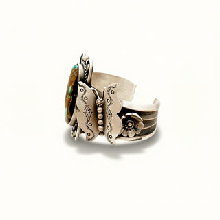 Silver cuff with intricate designs and a central gemstone on a white background