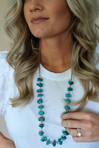 Woman wearing a long turquoise beaded necklace with a white top.