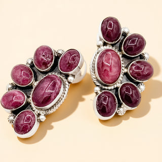 Pair of earrings with red gemstones and silver accents on a beige background