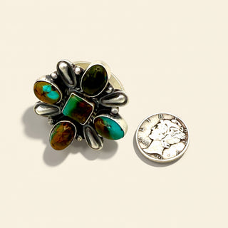 Silver brooch with green and brown stones next to a U.S. quarter on a beige background