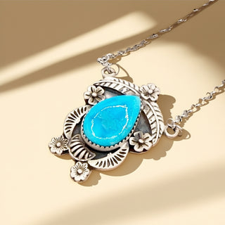 Necklace with a turquoise stone and silver floral design on a beige background