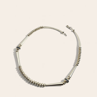 A silver-toned beaded chain necklace with alternating smooth cylindrical beads and coiled spiral beads, displayed on a light cream background.